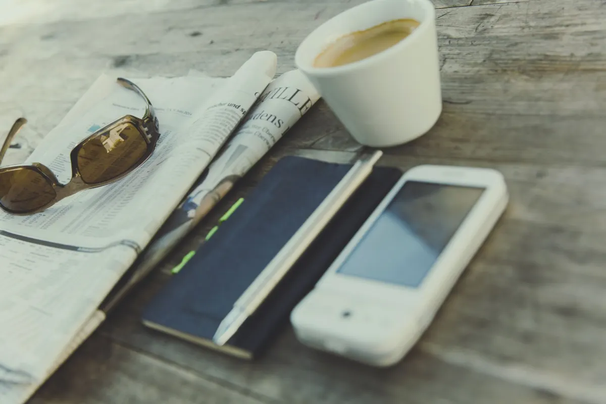 Un lector consulta una noticia en su smartphone en una mesa de cafetería, parte de la audiencia que el análisis de editores intenta captar.