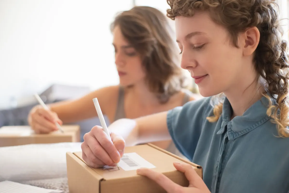 La propriétaire d'une petite boutique en ligne prépare des colis sur une table, le type de boutique dont les chiffres de revenu et de coût alimentent les métriques de marge et de remise.