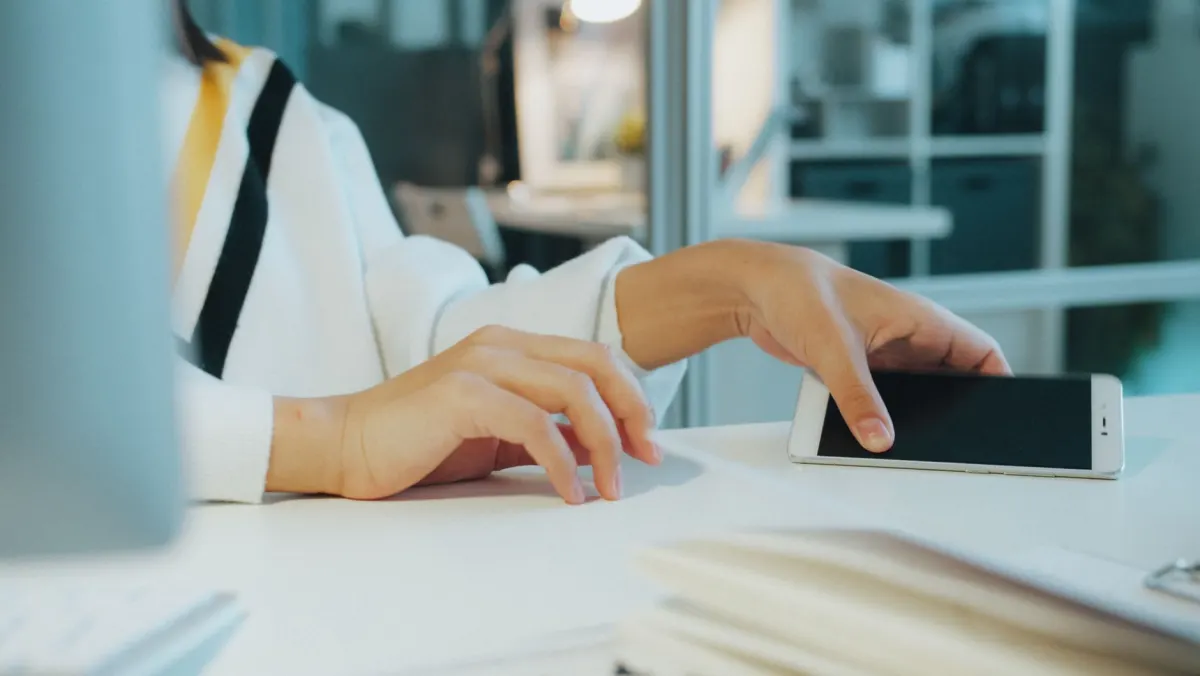 A person checking a smartphone at a desk, representing someone trying a new invite-only app on their phone.
