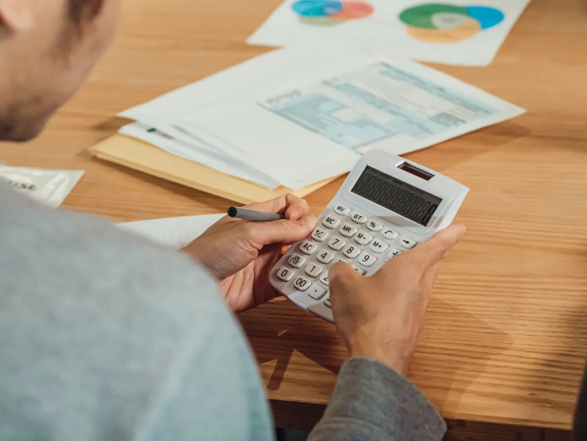 Una persona calcula porcentajes en papel junto a un portátil, la comprobación manual necesaria antes de confiar en una proporción de (not set).