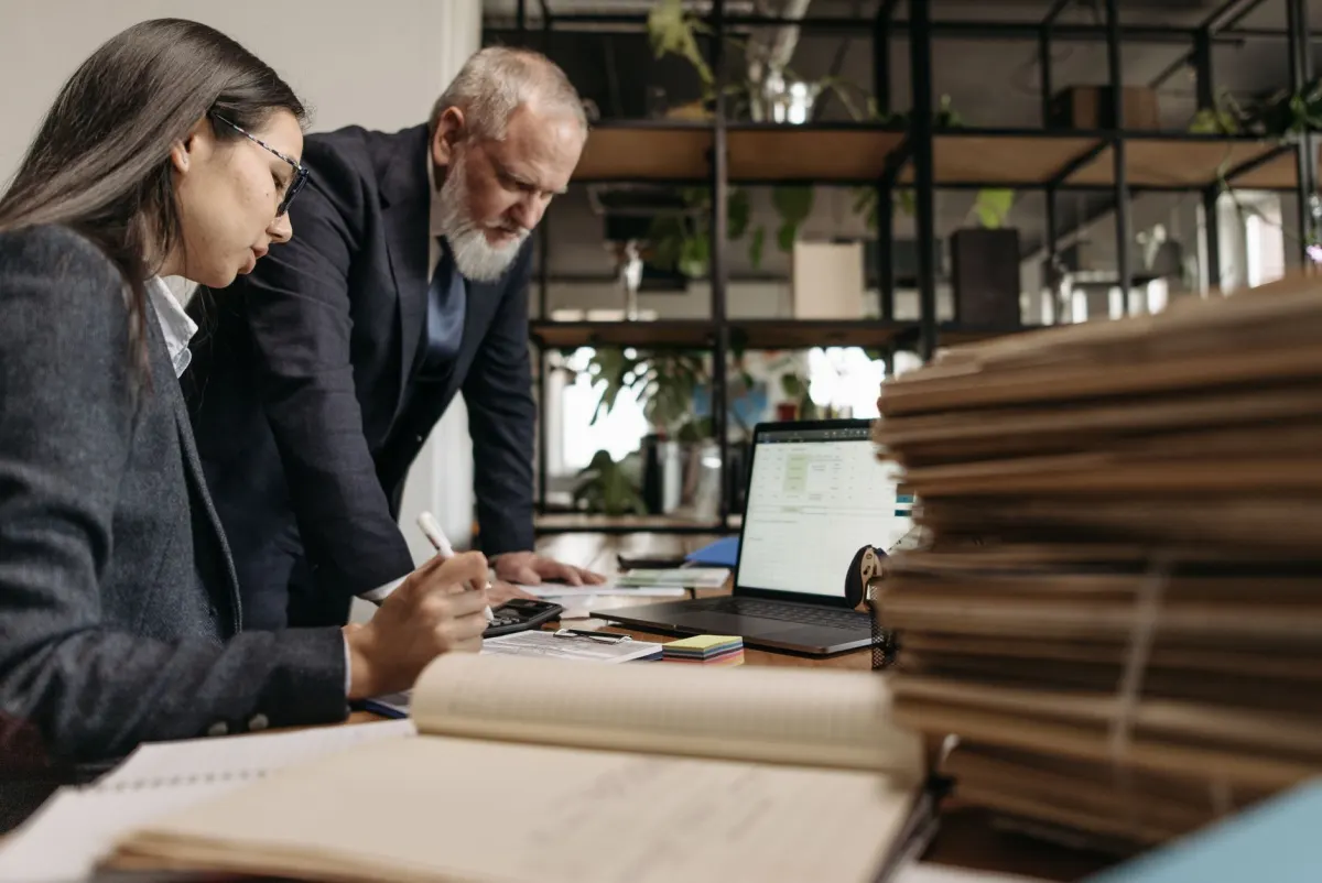 Two colleagues review a checklist on a laptop before deciding which pages to record.