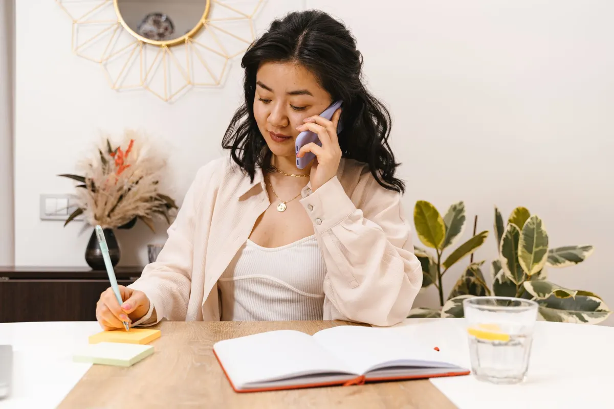 A person takes notes during a phone call, preparing questions to ask a software vendor.
