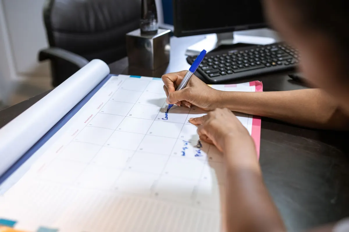 Un analyste note des chiffres hebdomadaires près d'un calendrier de bureau pour consigner une référence pour un site ecommerce.