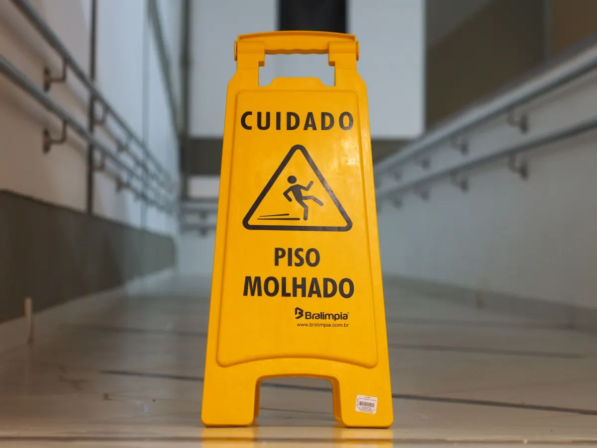 A yellow caution sign standing in a corridor that people can still walk through, like a label that warns without removing anything.