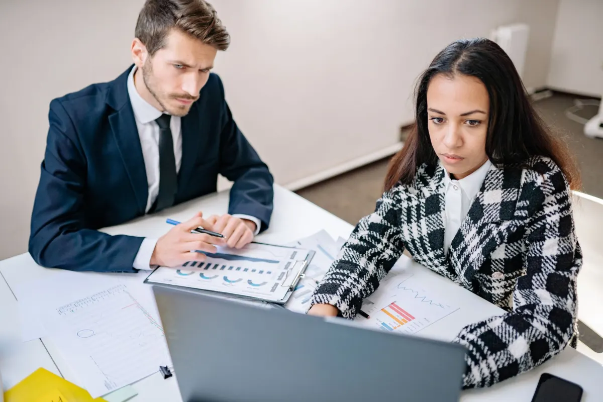 Dos compañeros revisan una laptop juntos, como un equipo que lleva la publicación y el monitoreo al mismo tiempo.