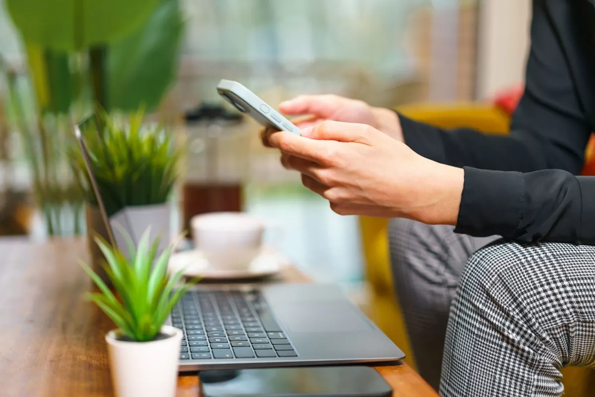 A person typing on a laptop while checking a phone, representing someone posting a question in a public forum thread.