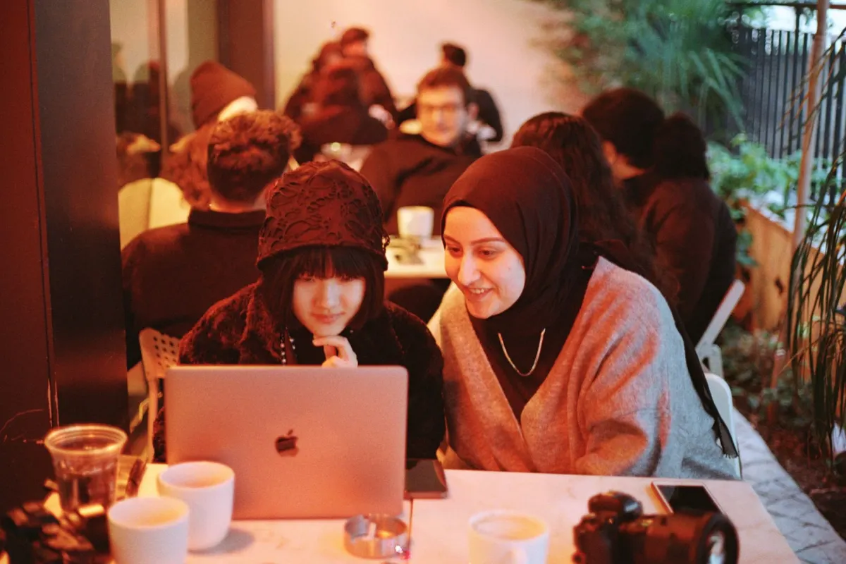 Two people compare notes on a laptop, evoking members answering each other's questions instead of waiting on staff.