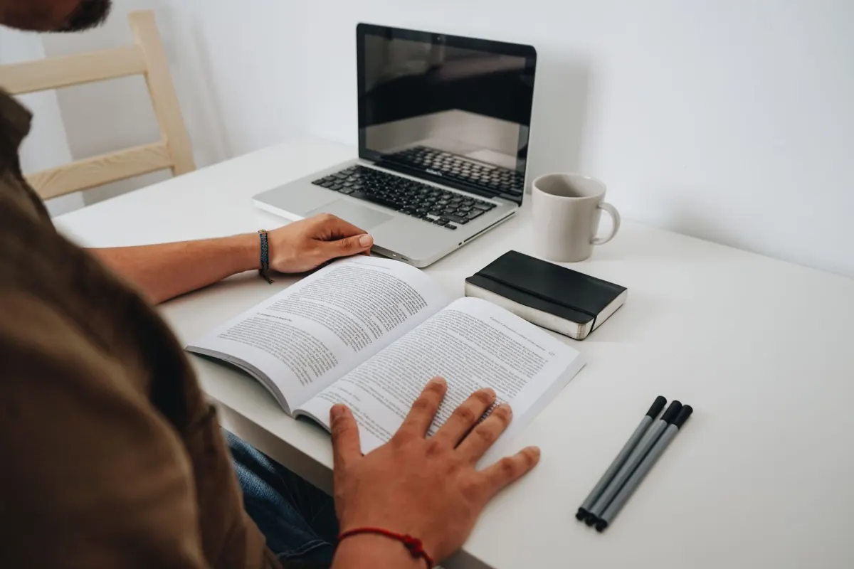 Eine Person scrollt an einem Laptop durch ein Onlineforum und macht sich Notizen in einem Notizbuch, wie es bei der hier beschriebenen Social-Listening-Recherche der Fall ist.