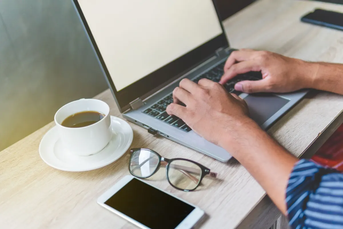 Eine Person tippt neben einer Kaffeetasse auf einem Laptop, als Bild für die Morgenroutine, in der der Reddit-Digest des Agenten ankommt.