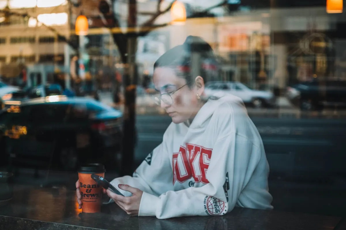 A woman scrolls through a phone in a cafe, the kind of moment where someone types a question about which product to buy.