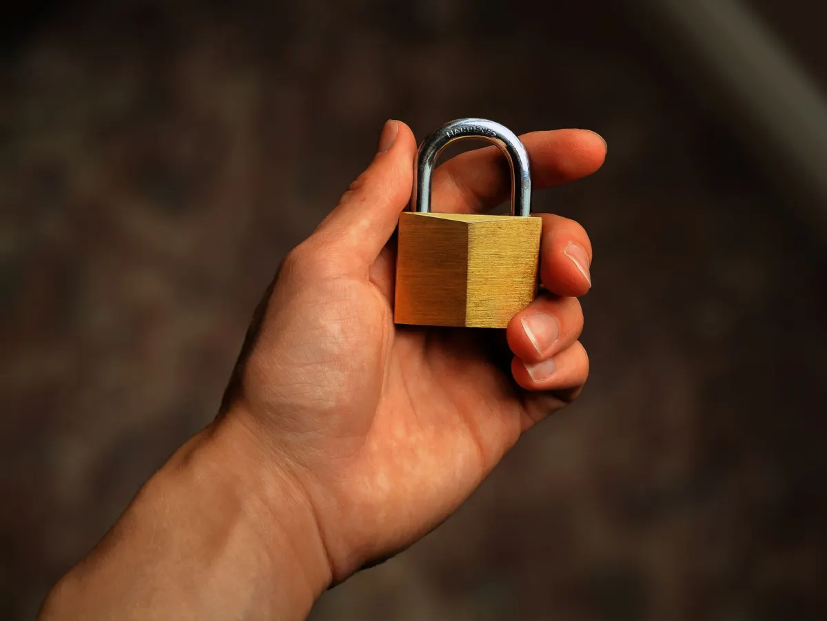 A hand resting near a closed padlock, showing why credentials belong in the sign-in window and not in a chat message.