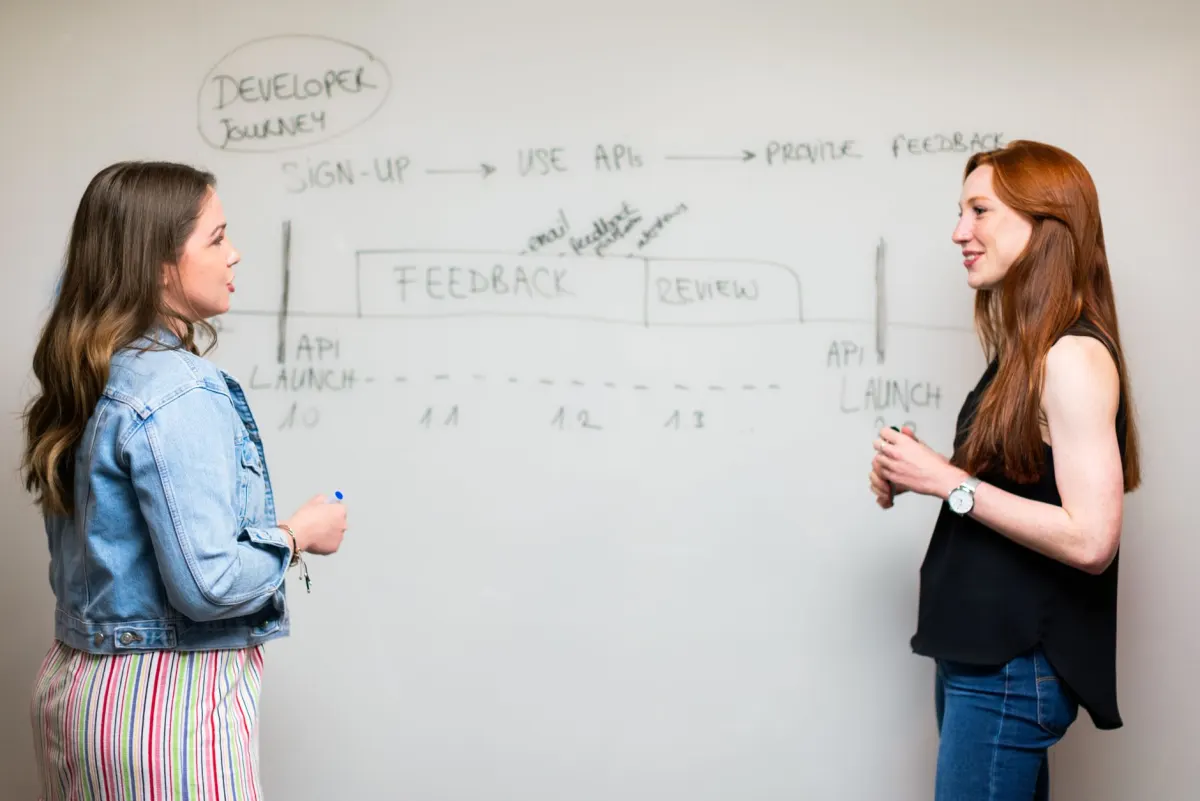 Two colleagues discussing feedback at a whiteboard, evoking the tone of curiosity and respect expected in a Show HN thread.